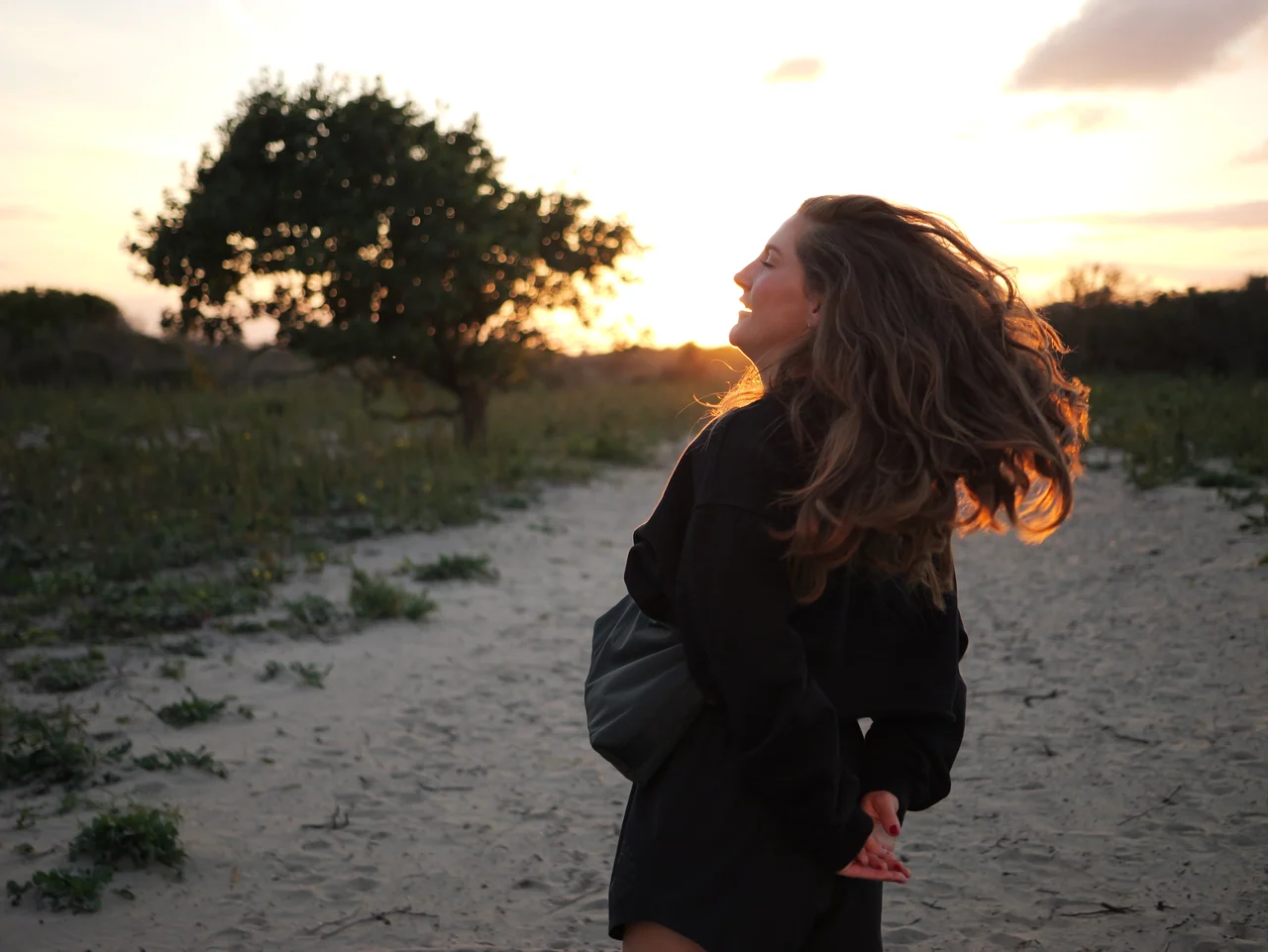 Een vrouw draait in de duinen, haar haar verlicht door de ondergaande zon